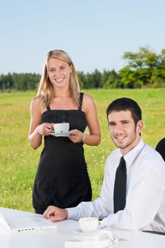 Young businessman in sunny nature have coffee with female colleague