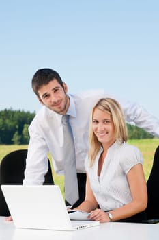 Young business colleagues in nature office smile behind table