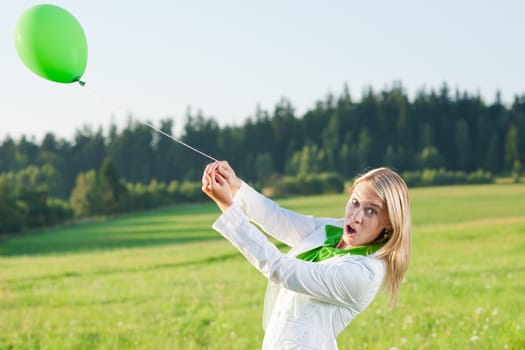 Happy young woman with green balloon in sunny meadows nature