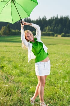 Happy young woman with green umbrella in sunny meadows nature
