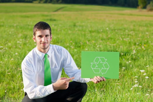 Green energy - Young businessman in sunny meadows hold recycling sign