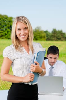 Young businesswoman in sunny nature with folders and male colleague