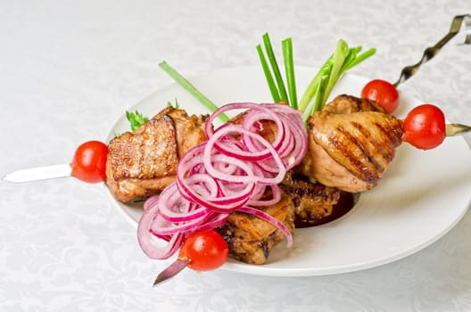 Grilled kebab meat with onion and tomato on a white plate