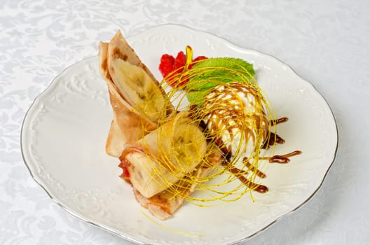 Dessert of pancake with banana, ice-cream, caramel, strawberry and mint
