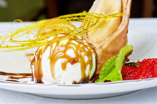 Dessert of pancake with banana, ice-cream, caramel, strawberry and mint