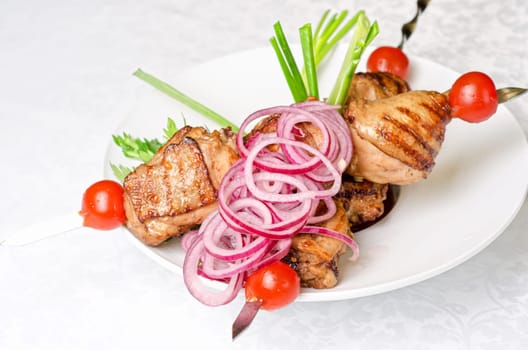Grilled kebab meat with onion and tomato on a white plate