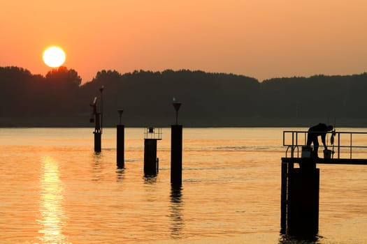 Orange and foggy sunset at the riverside with fisherman