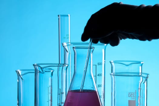 Laboratory technician working with laboratory glassware - chemical flasks with one colored solution.