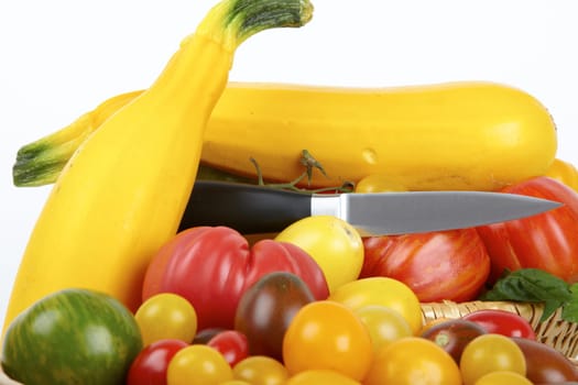 Fresh tomatoes and yellow zucchinis with knife in basket