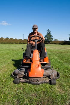 Mature man driving grass cutter in a sunny day
