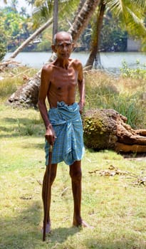 Kerala, India -  September 25, 2011: Indegenous old man with walk stick and traditional blue loin cloth, full length with crop margins