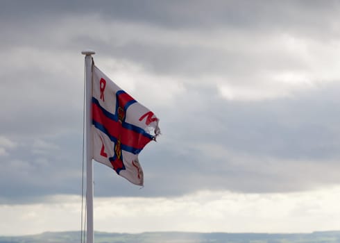 Worn flag of the Royal National Lifeboat Institution blows in the wind on a cloudy day