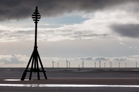 Wind turbines in the ocean off a sandy beach near Liverpool on a cold and cloudy day