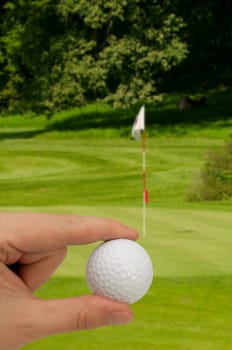 Hand Holding Golf Ball - Golf Green With Flag in Background