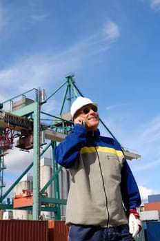 port worker talking in phone, container-crane and dock in background