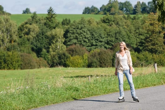Inline skating young woman wearing jeans on sunny asphalt road