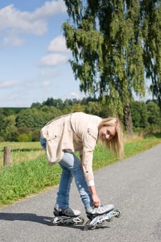 Young woman tightening inline skates on sunny asphalt road