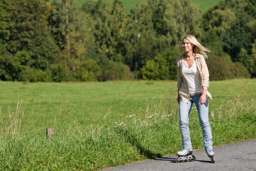 Inline skating young woman wearing jeans on sunny asphalt road