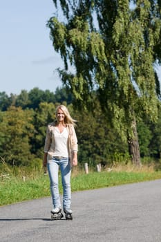 Inline skating young woman wearing jeans on sunny asphalt road