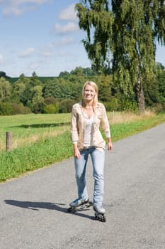 Inline skating young woman wearing jeans on sunny asphalt road