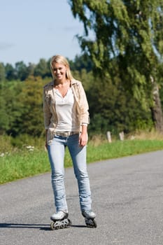 Inline skating young woman wearing jeans on sunny asphalt road