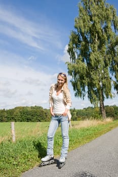 Inline skating young woman wearing jeans on sunny asphalt road