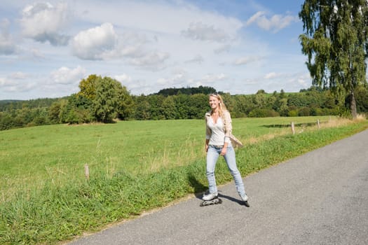 Inline skating young woman wearing jeans on sunny asphalt road