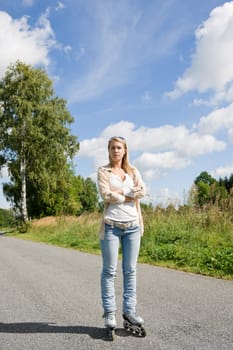 Inline skating young woman wearing jeans on sunny asphalt road