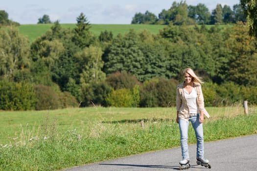 Inline skating young woman wearing jeans on sunny asphalt road
