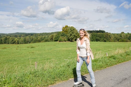 Inline skating young woman wearing jeans on sunny asphalt road