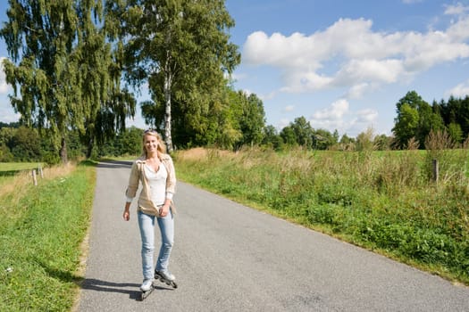 Inline skating young woman wearing jeans on sunny asphalt road