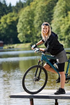 Mountain biking young woman standing on pier looking natural lake
