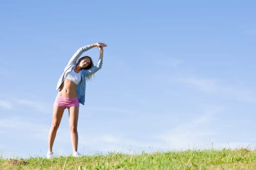 Sportive stretching young happy woman meadows blue summer sky