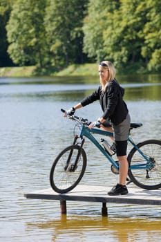 Mountain biking young woman standing on pier looking natural lake