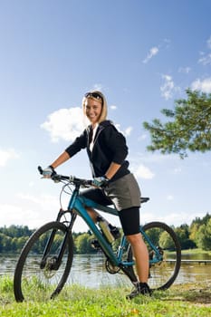 Beautiful young blond woman riding bicycle by lake summer day