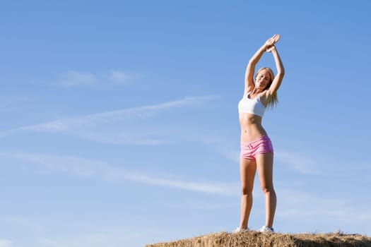Summer active woman stretching on bales in fitness outfit