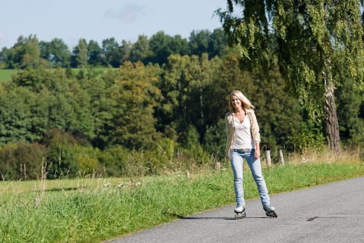 Inline skating young woman wearing jeans on sunny asphalt road