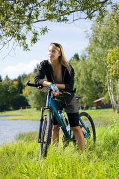 Beautiful young blond woman riding bicycle by lake summer day