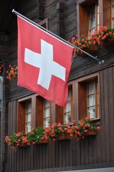 foreshortening of ancient building wooden facade with geranium and red swiss flag