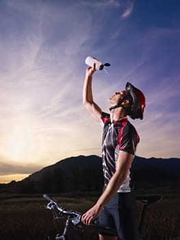 sports activity: young adult cyclist on mountain bike spilling water on face from bottle. Vertical shape, side view, copy space