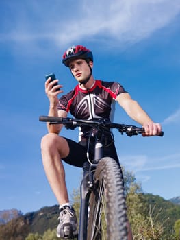 sports activity: young adult cyclist riding mountain bike and text messaging on cellphone. Vertical shape, low angle view
