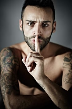 portrait of proud young adult man with tattoos hissing. Vertical shape, front view, studio shot