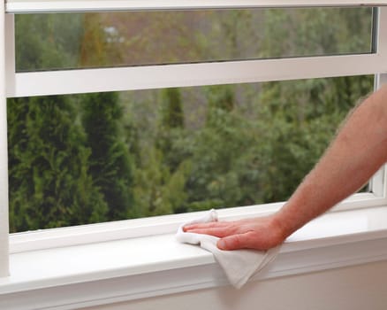 Hand dusting a window sill to reduce allergens in the home.