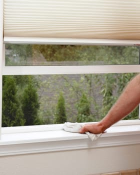 Male hand wiping off a window sill to reduce allergens in the home.