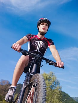 sports activity: young adult cyclist riding mountain bike in the countryside. Vertical shape, low angle view, copy space