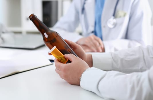Alcoholic hold in hand empty bottle at doctor reception office closeup. Grief and despair intoxicated change life drunkenness lifestyle sobriety and temperance bad habit dependence concept