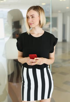 Business woman holding a smartphone in her hands reflection in the glass of red color is trying to call while working break the blonde