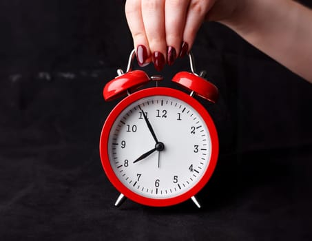 Female arm hold up red alarm clock dial on black background with five before eight oclock early morning closeup
