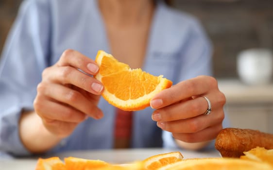 A woman holds a slice of sliced orange in her hand during an early breakfast in the kitchen the concept of a healthy diet