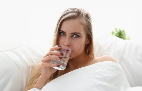 beautiful young blond woman hold glass of water in arm early morning stay in bed
